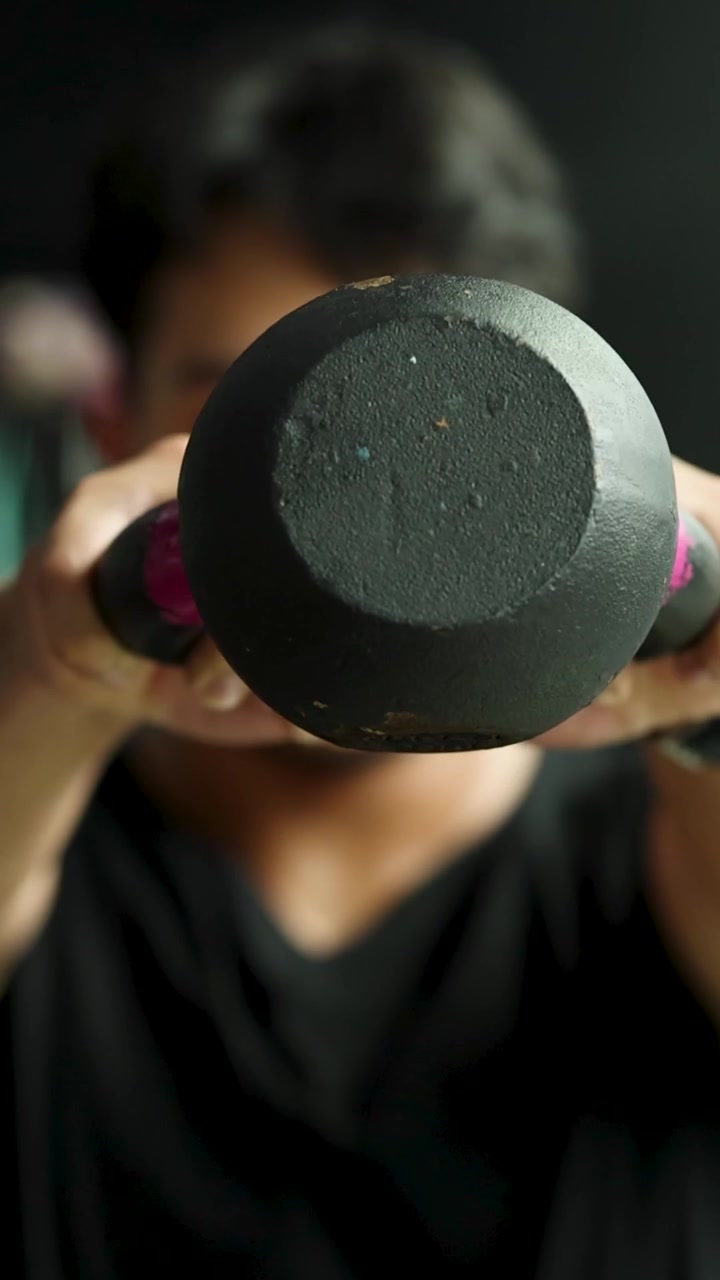 Un uomo concentrato esegue oscillazioni ritmiche con il kettlebell in un primo piano verticale in palestra.