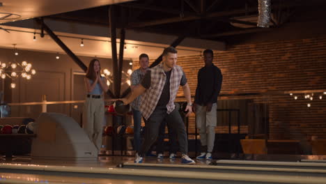 A-young-man-throws-a-bowling-ball-and-knocks-out-a-shot-with-one-throw-and-hugs-and-rejoices-with-his-friends.-Multi-ethnic-group-of-friends-bowling