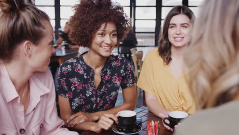 four young female friends meeting sitting at table in coffee shop talking