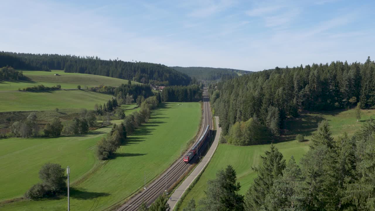 un tren viajando a través de un valle exuberante y verde flanqueado por densos bosques, vista aérea
