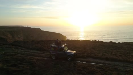 aerial of cute couple four by four vehicle along ocean cliffs at sunset