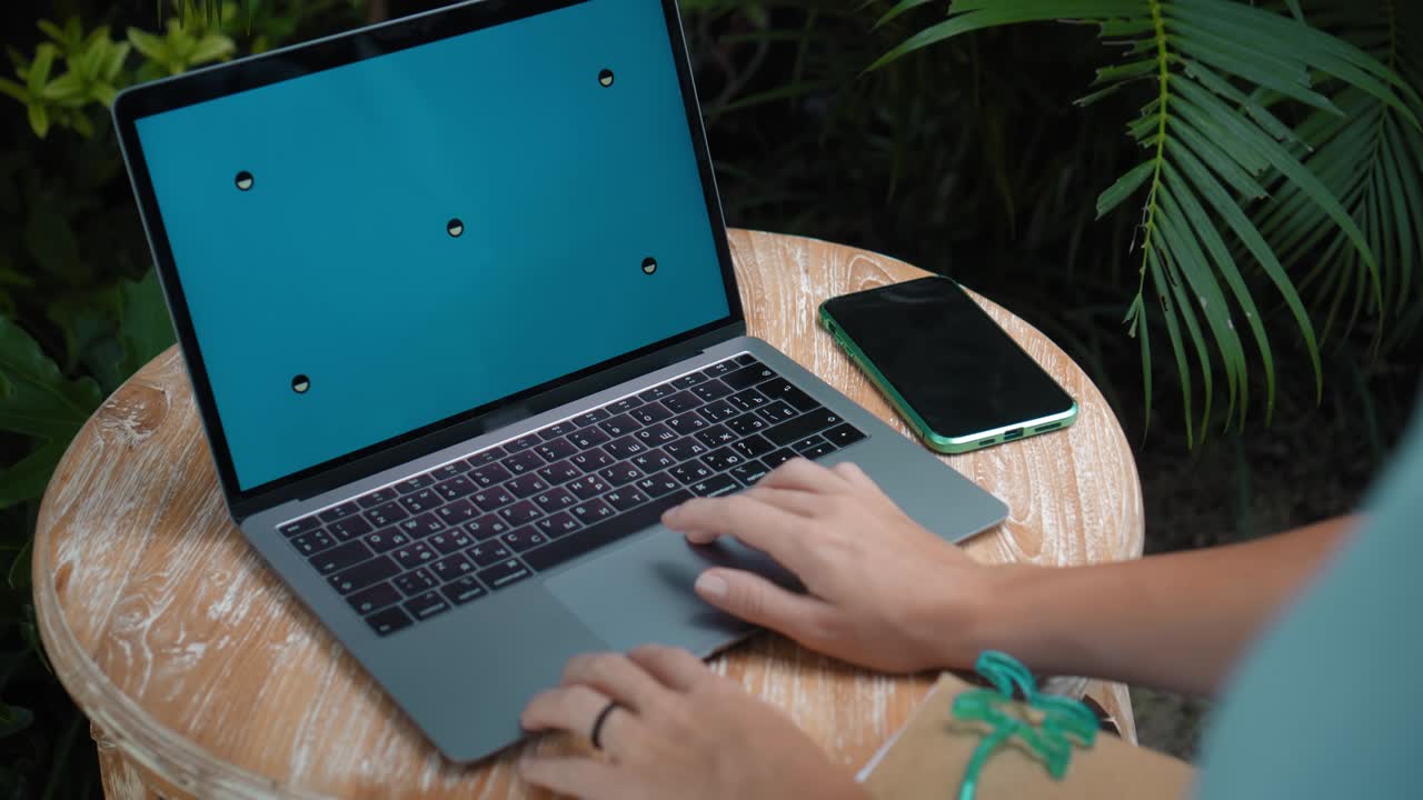 un joven europeo en un vestido azul remotamente en línea trabajando en una computadora portátil con pantalla azul en el patio trasero con plantas verdes