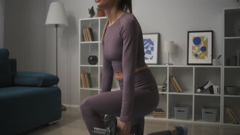 tired woman is squatting with dumbbells in hands working muscles of legs and ass wellness and healthy lifestyle training in living room