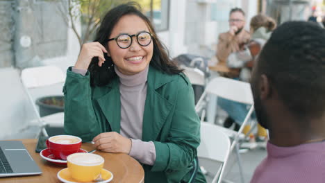 Alegre-Mujer-Asiática-Hablando-Con-Un-Hombre-Afroamericano-En-Un-Café-Al-Aire-Libre