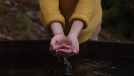 female cups water in hands in nature