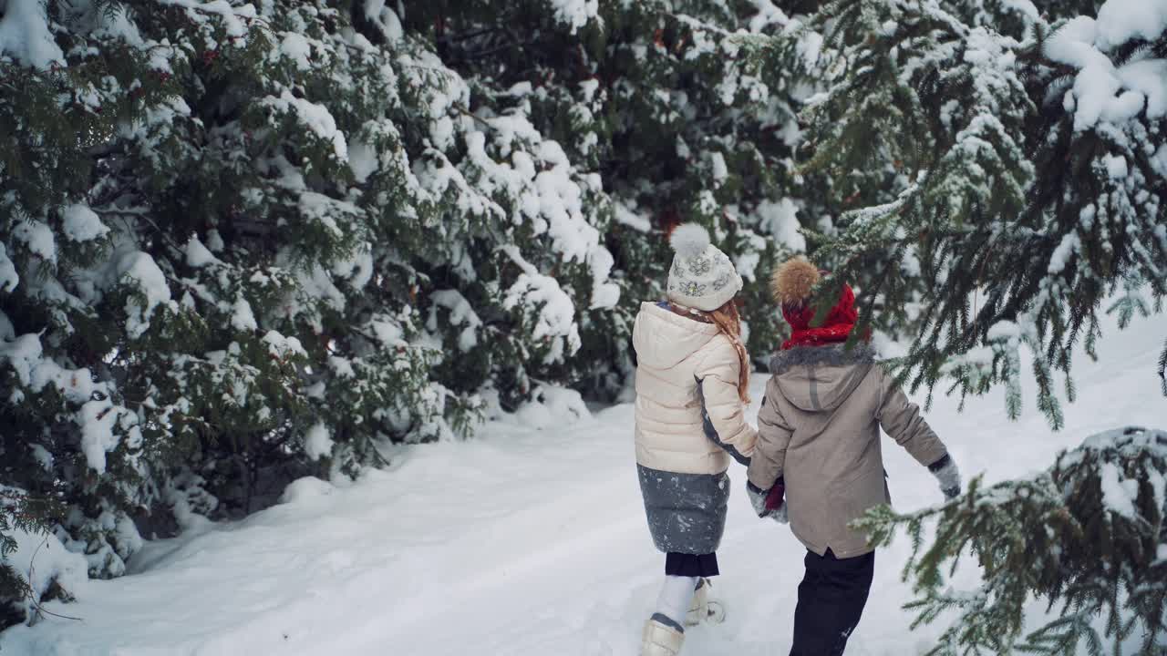 Back view of two kids in the forest in winter. Children with envelope trying to find the way to Santa on the snowy background outdoors.
