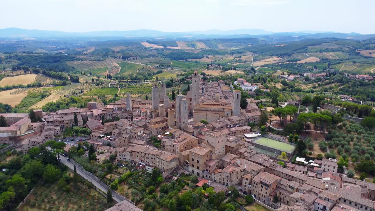 Wide aerial view of San Gimignano’s medieval skyline surrounded by rolling Tuscan vineyards and hills, captured from a high drone perspective.