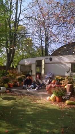 two women relaxing by a camper trailer in an autumn garden