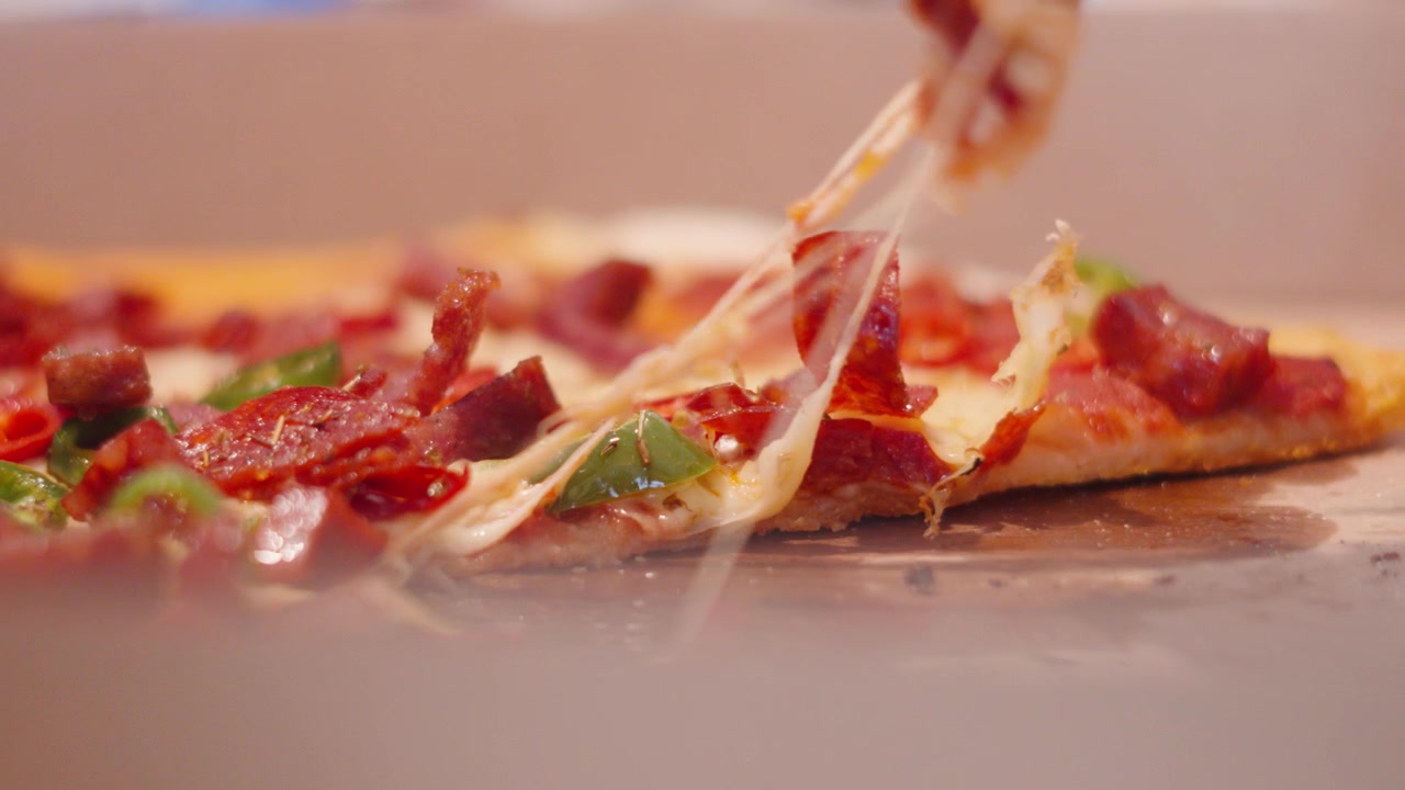 Afferrare una fetta di pizza con formaggio filante e condimenti di carne come pepperoni e peperoncini.
