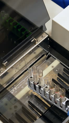 gloved hand of a laboratory expert puts the stand with test tubes into equipment. machine for blood test analysis in modern hospital. vertical video