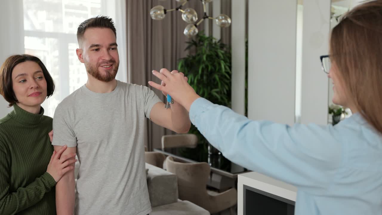 un agente de bienes raíces está dando llaves a los compradores de un nuevo apartamento. una pareja de jóvenes clientes alquilan una inversión. comprar un concepto de casa.