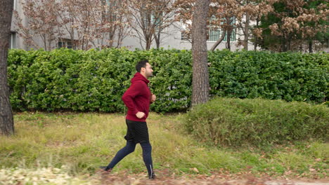 profile of sporty man in 30s jogging in a park in autumn - tracking motion