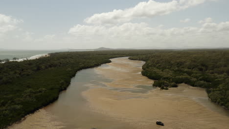 Toma-Aérea-Hacia-Atrás-De-Automóviles-Conduciendo-En-Playas-De-Arena-Y-Piscinas-De-Agua-Rodeadas-Por-El-Paisaje-Forestal-De-Queensland-En-Australia