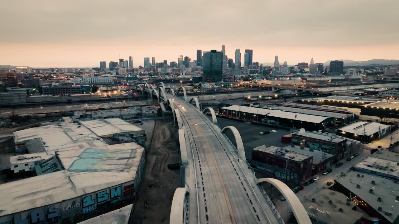 A retreating drone shot of the Ribbon Of Light 6th Street Bridge during sunset in Los Angeles California with cars driving in the foreground of the city's skyline, moving backwards