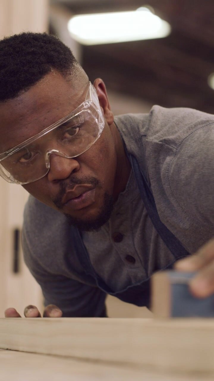 Focused Carpenter Sanding Wood Plank in Workshop