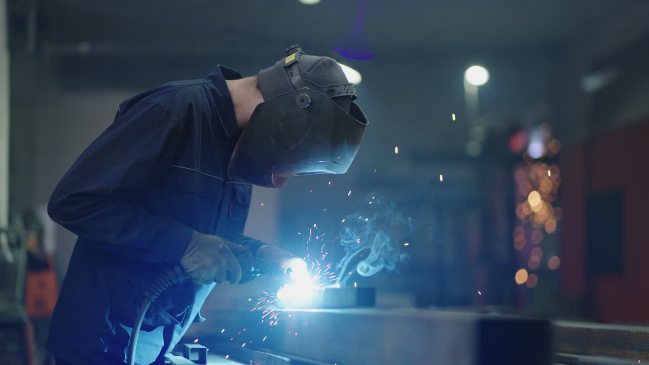 welding work at a metalworking plant. A helmet welder welds a metal part on a welding table. Welding of steel sparking not wearing gloves light colored like fireworks. Industrial Worker