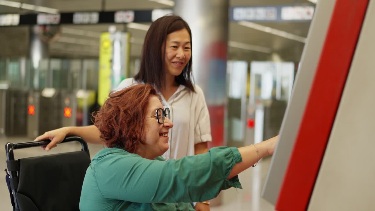 Woman in wheelchair using ticket machine with assistance