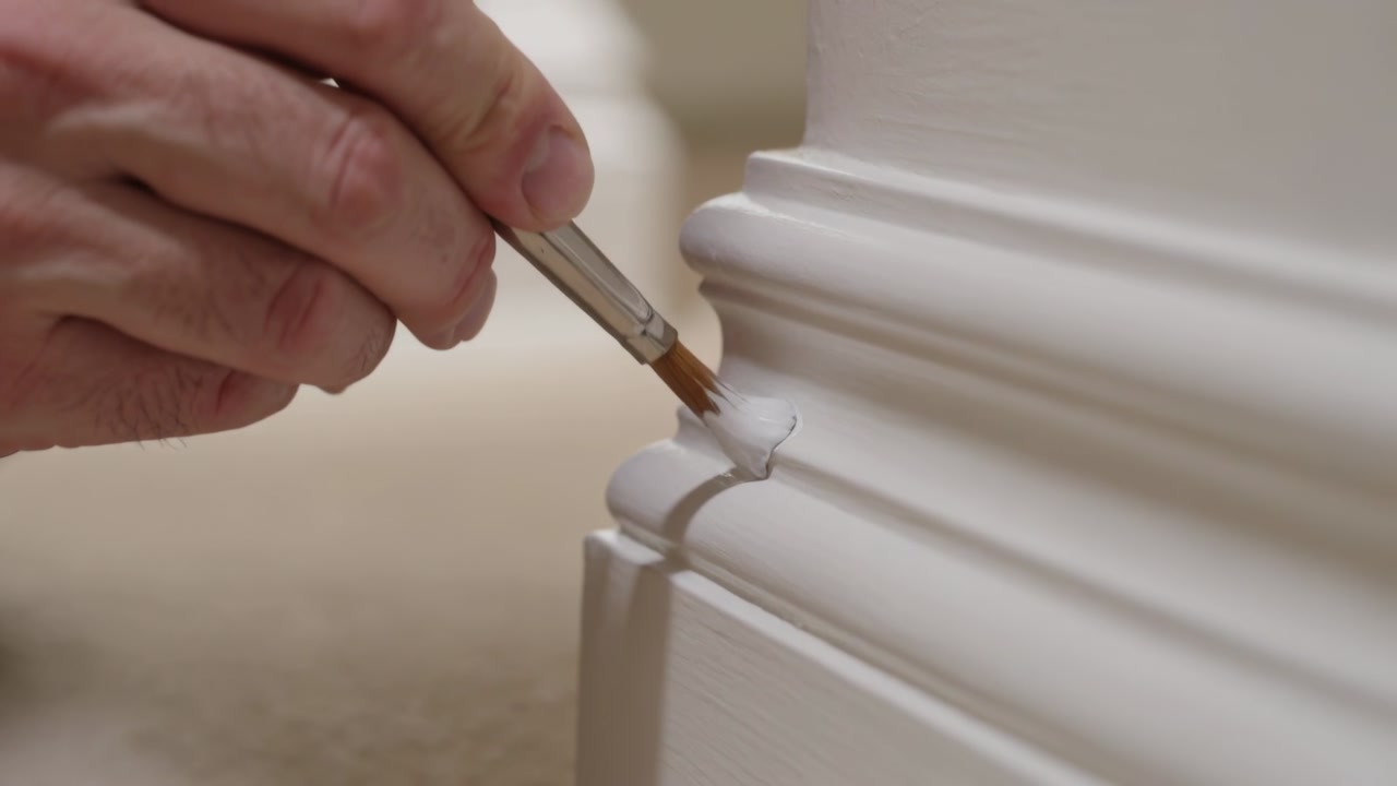 Dabbing adult hand touching trim groove with round brush, applying white paint for touch-up at home