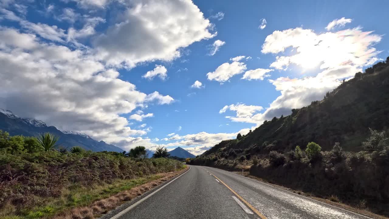 Vista frontal de un coche en una carretera rural, montañas, lago, nubes dinámicas, luz natural, movimiento fluido