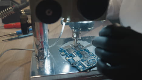 close-up view of a technician using a microscope to examine and repair a circuit board