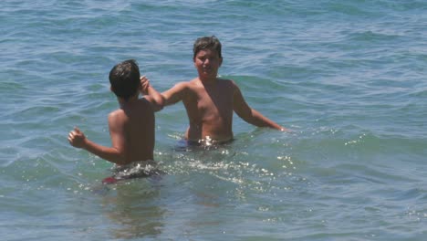 Imágenes-En-Cámara-Lenta-Media-De-100-Fps-De-Dos-Hermanos-Caucásicos-Chocando-Los-Cinco-En-El-Mar,-Disfrutando-De-La-Natación-Durante-Sus-Vacaciones-De-Verano