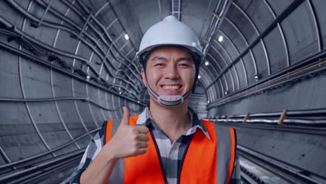 Close Up Of Asian Male Engineer With Safety Helmet Smiling And Showing Thumbs Up Gesture To The Camera While Standing In Underground Subway Tunnel