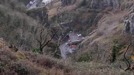 Red-car-driving-and-weaving-through-Cheddar-Gorge-valley-landscape-in-rural-countryside-town-of-Cheddar-in-Somerset,-England