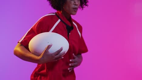 african american female rugby player running with rugby ball over neon pink lighting