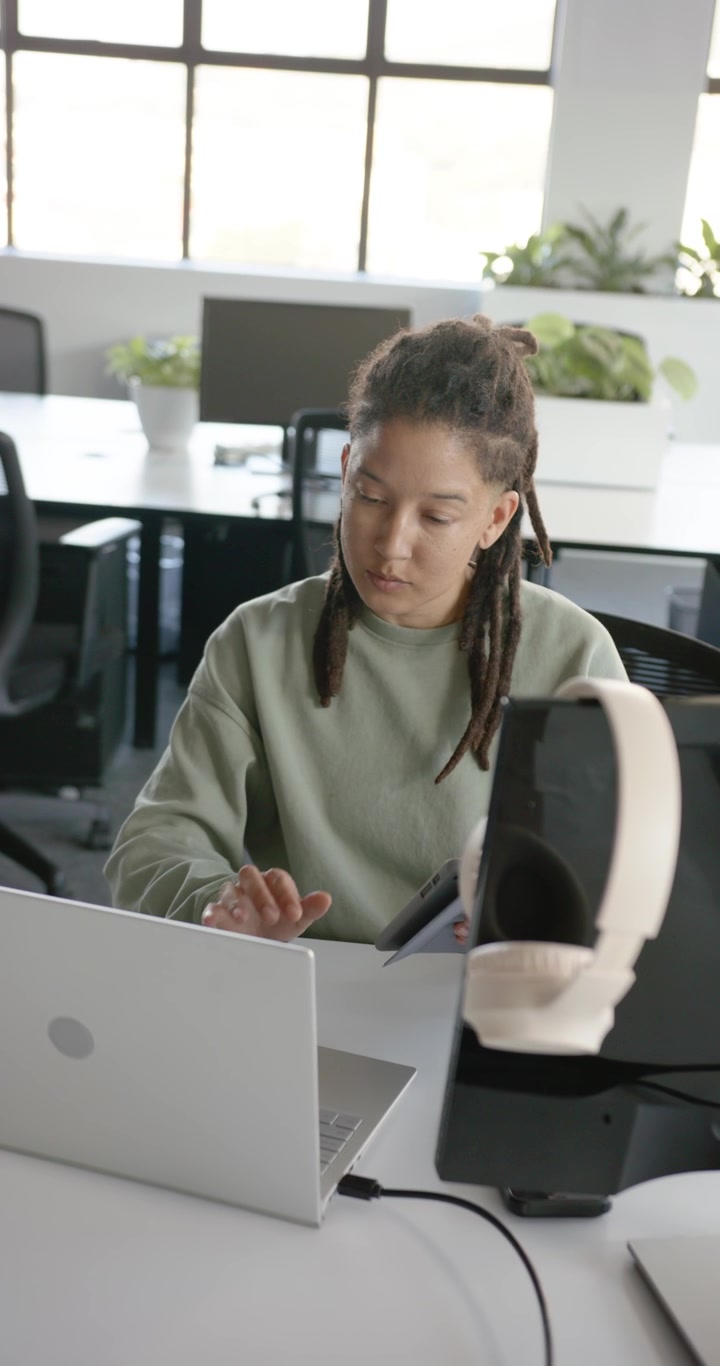 Video verticale: Persona lavoratrice africana non binaria che guarda il laptop, digita, tocca il tablet e si destreggia tra le attività lavorative.