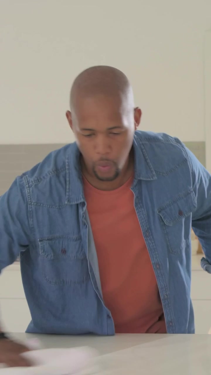 Vertical video: Reaching for white cloth, man in denim shirt wiping kitchen island for cleaning