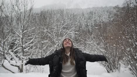 content woman in outerwear outstretching arms in winter forest