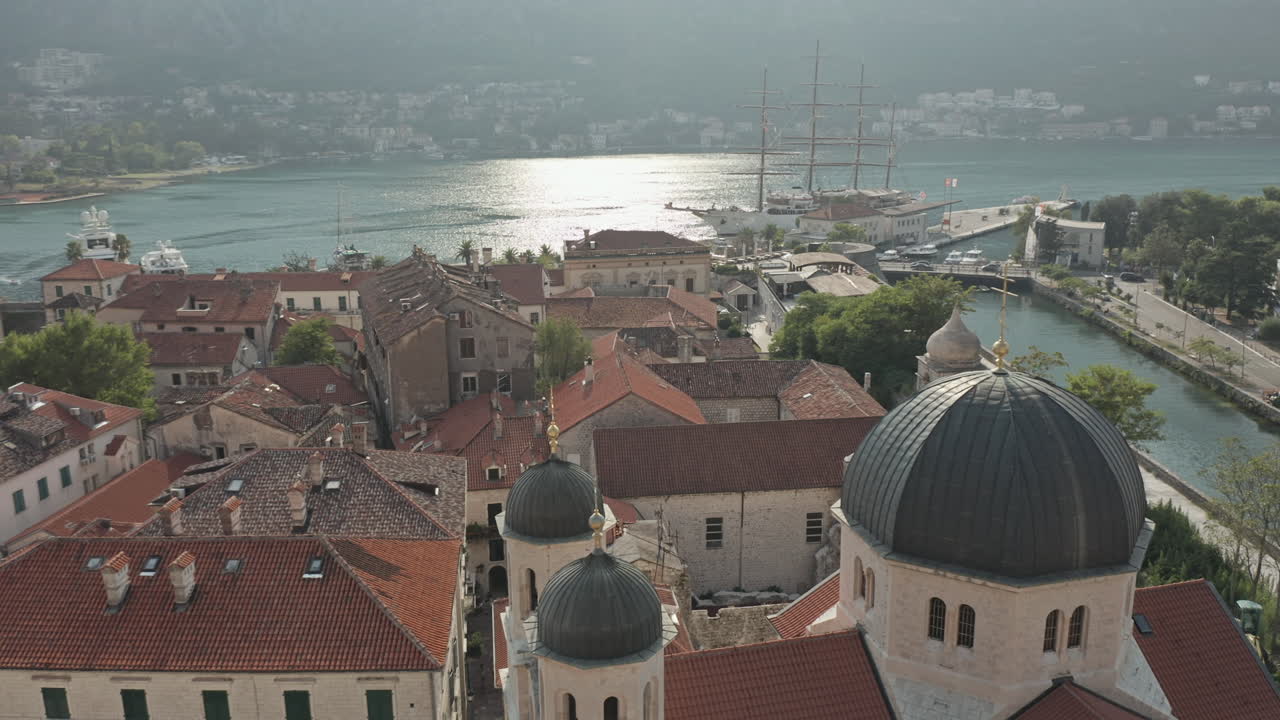 Mid-day parallax drone shot of Kotor, Montenegro church with view of the bay and giant ship