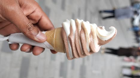 close-up of a hand holding a chocolate and vanilla swirl soft-serve ice cream cone
