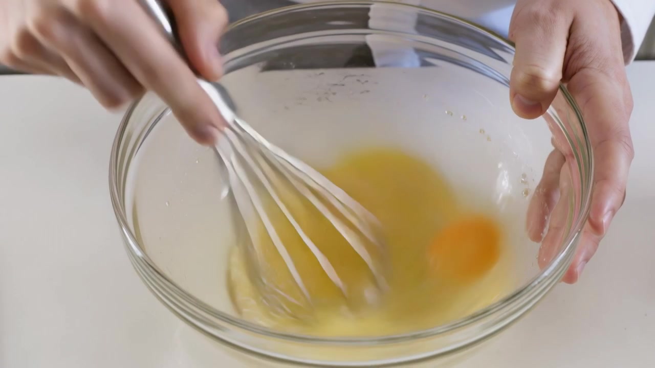 Placing metal whisk, cook wearing white coat holding clear bowl in kitchen whisking eggs for omelet