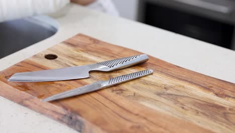 A person arranges knives on a wooden cutting board in a well-lit kitchen setting