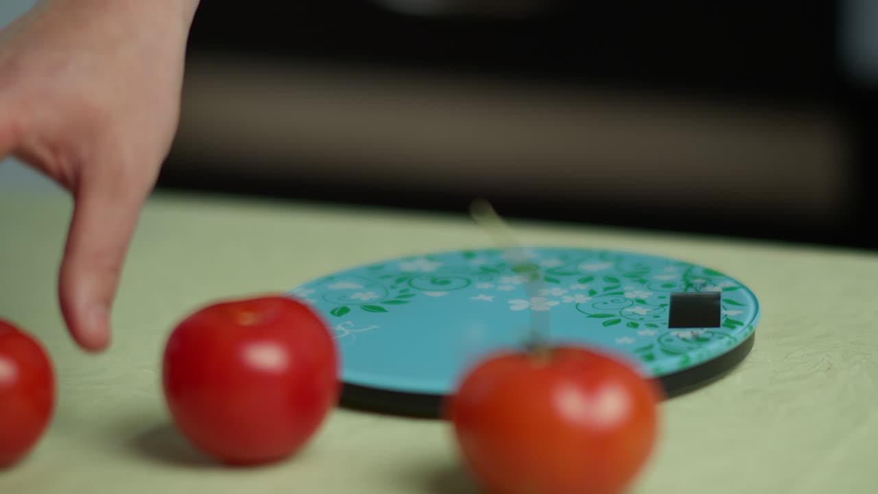한 남자가 주방 스케일에서 몇 개의 신선한 토마토를 가중합니다.