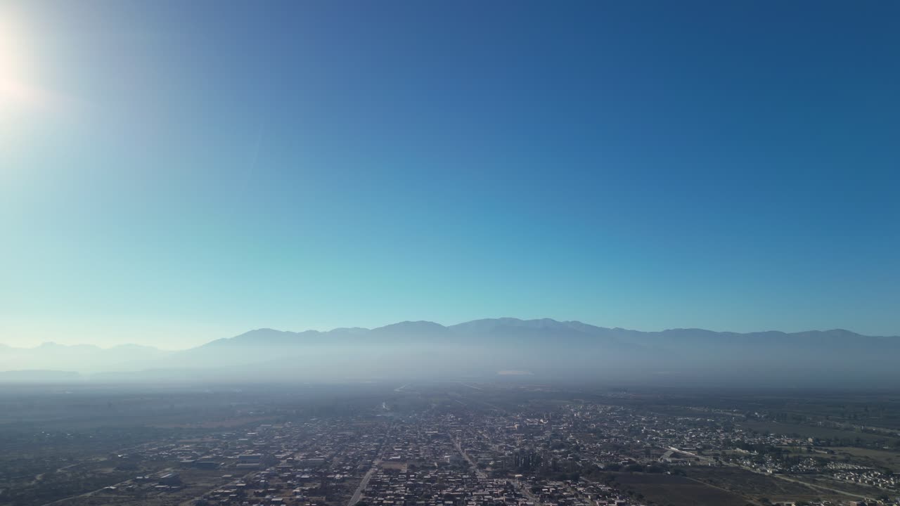 Luftfoto af by i dal med bjerge og klar, blå himmel
