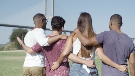 back view of smiling friends hugging and walking on meadow.