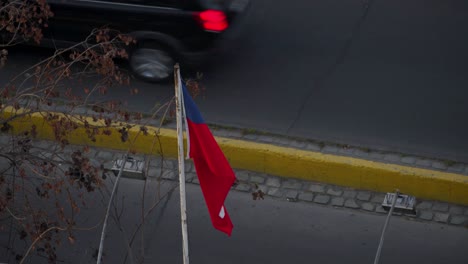 bandera de chile ondeando en el viento con vehículos que pasan en segundo plano