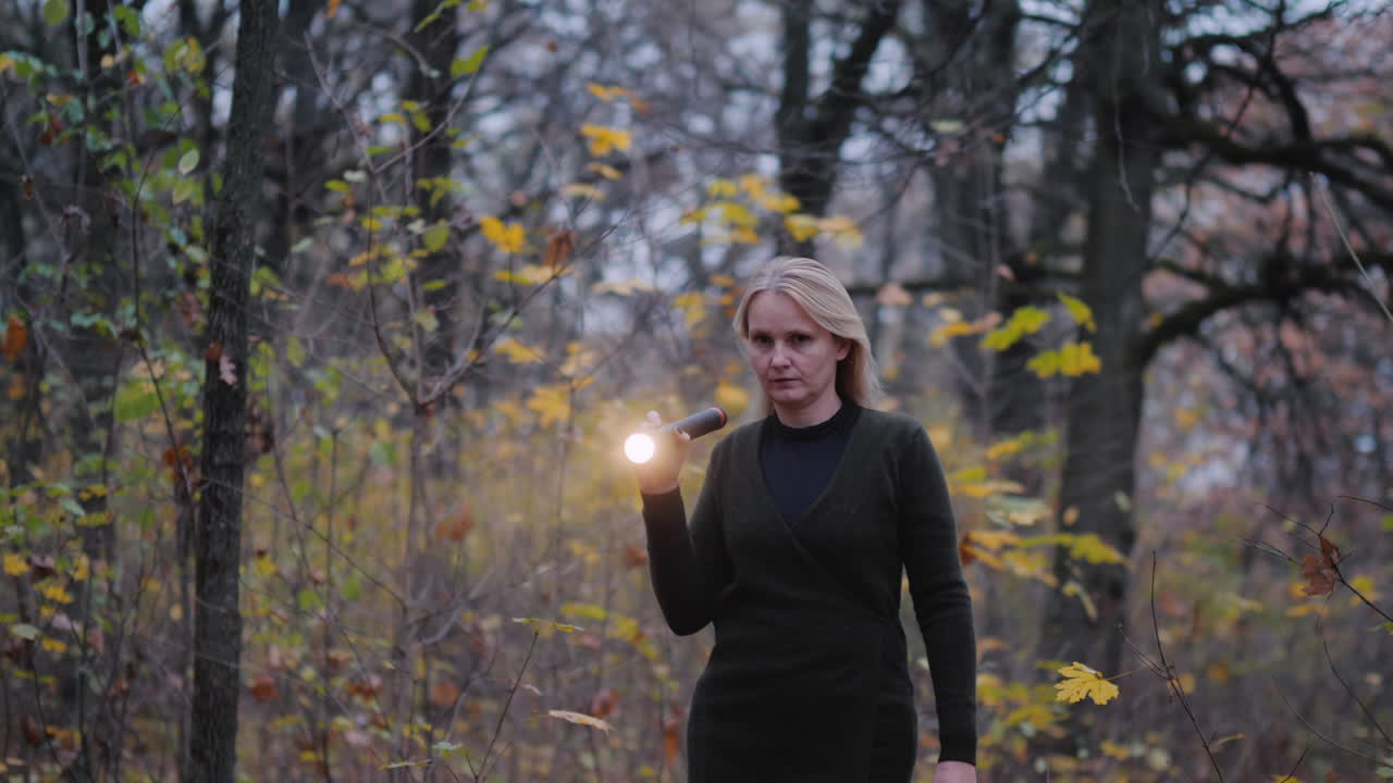 una mujer con una linterna en la mano camina por el bosque al atardecer