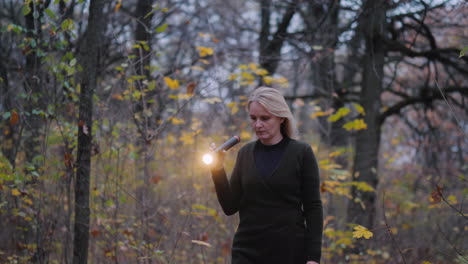 a woman with a flashlight in hand walks through the woods at dusk