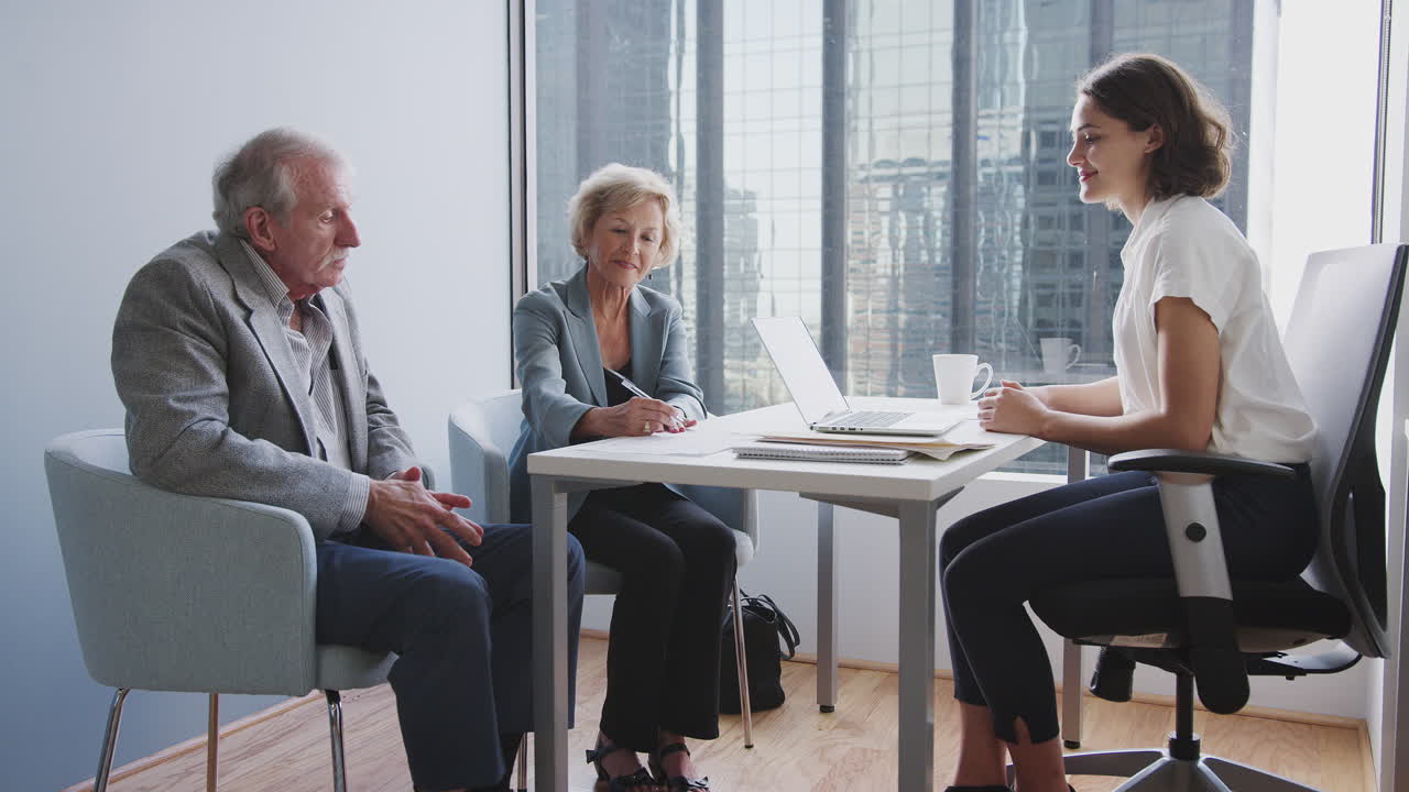 Senior Couple Signing Document In Meeting With Female Financial Advisor In Office