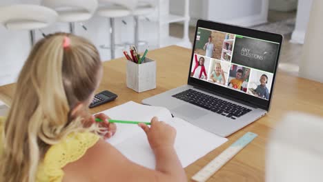 Schoolgirl-using-laptop-for-online-lesson-at-home,-with-diverse-teacher-and-class-on-screen