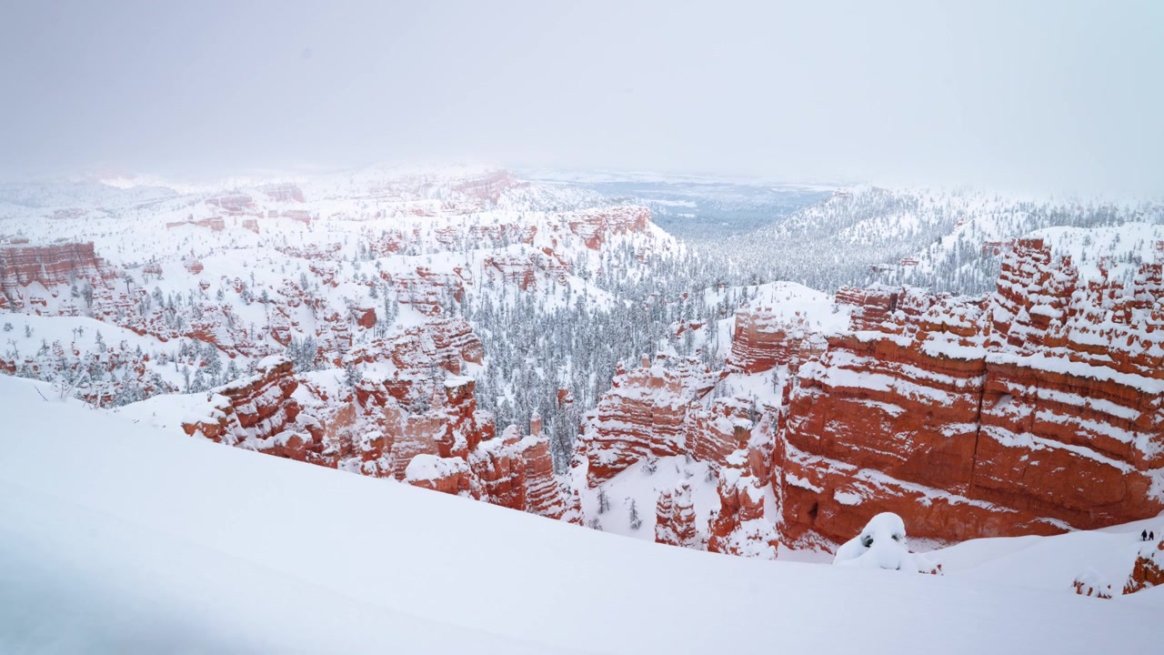 Upea laajakuva Bryce Canyonin kansallispuiston punaisista Hoodoo-kivimuodostelmista, joita peittää paksu lumikerros luoden sumuisen tunnelman kanjoniin.