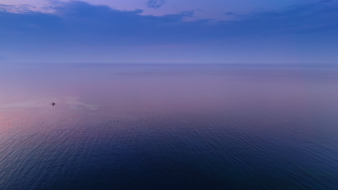 Endless seascape colored pink at the time of sunset. Little light sign splashes in the water