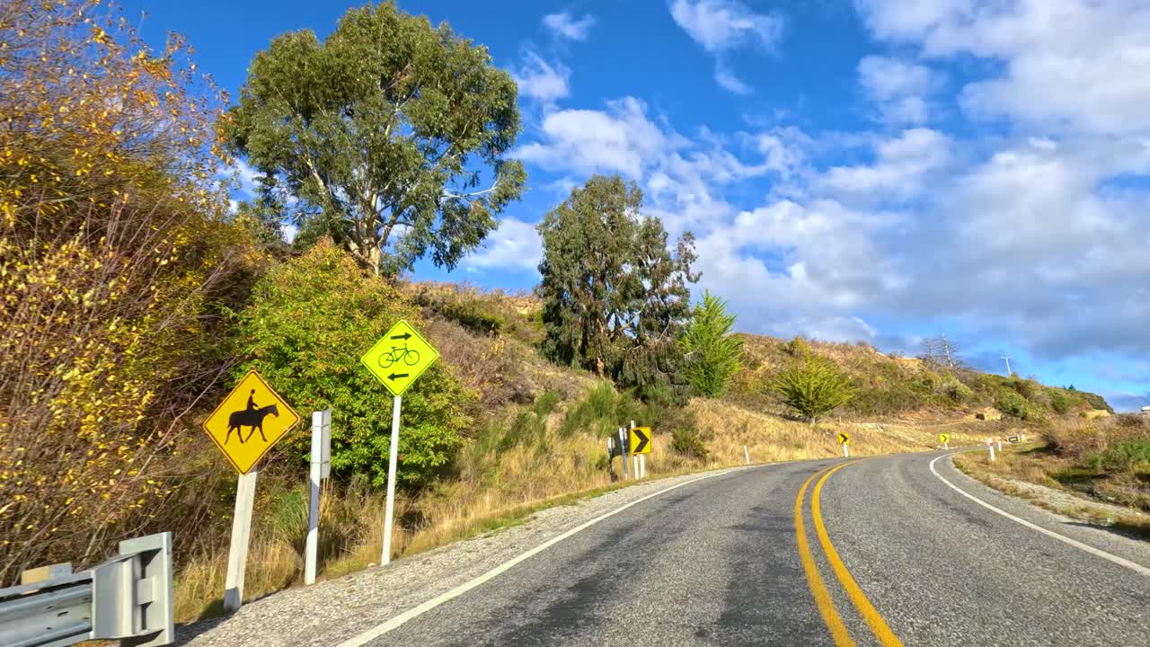 Vehicle drives winding rural road through scenic autumn landscape, bright daylight, smooth camera, clear sky