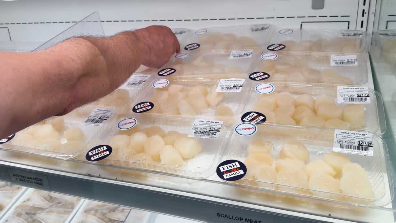 A customer picks up a plastic container of fresh scallops from a grocery store refrigerator
