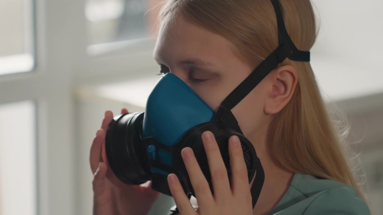 Donna in interni che regola con cura le cinghie del respiratore. Donna calma in una stanza illuminata dal sole che regola il dispositivo di protezione facciale. La proprietaria di casa che indossa con calma il respiratore alla luce del sole prima di una pulizia profonda e accurata.