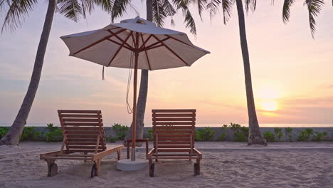 tropical island seashore on sunset and two deckchairs under a parasol near beach