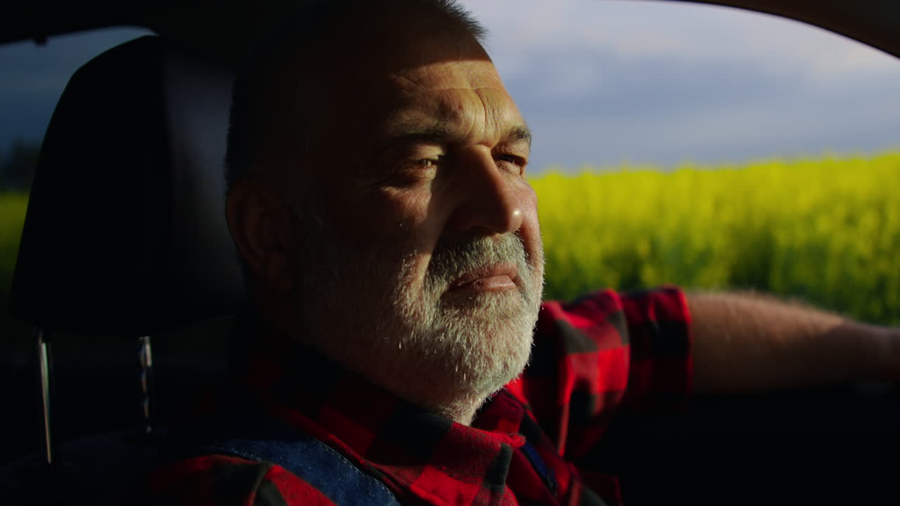 Mature Farmer Looking Out Car Window at Yellow Field